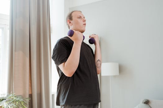 A young man lifting dumbbells in a home setting, focusing on personal fitness and health.