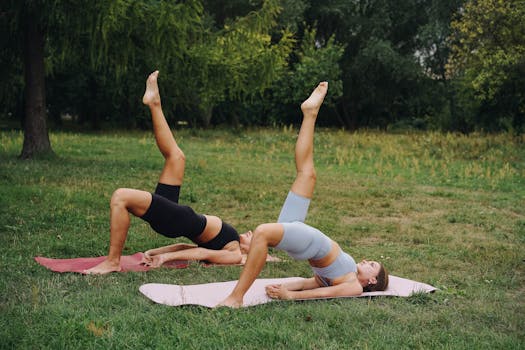 Two women practice yoga exercises on mats in a serene outdoor park, promoting fitness and well-being.